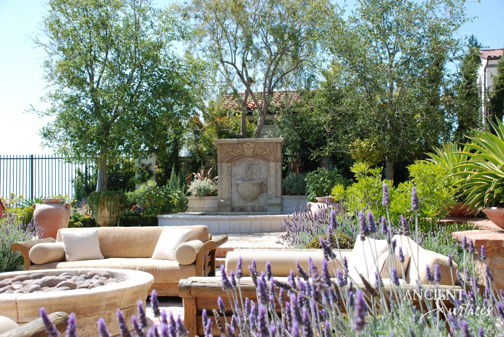 Antique reclaimed limestone wall fountain set on a lavender garden terrace with lush Mediterranean planting